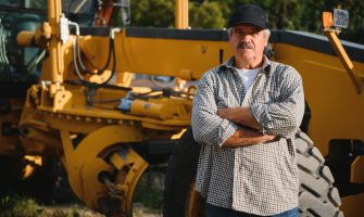 A professional driver stands on the background of a grader.